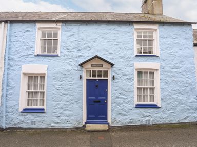 Exterior view of a light blue stone cottage with a blue door and four windows at Bwthyn Dwyfor in Beaumaris