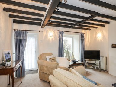 A living room with beige armchairs a glass coffee table and a television at Bwthyn Dwyfor in Beaumaris