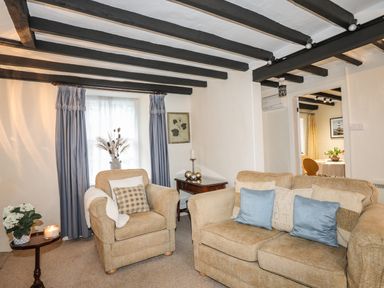 A living room with armchair sofa wooden side tables and blue curtains at Bwthyn Dwyfor in Beaumaris