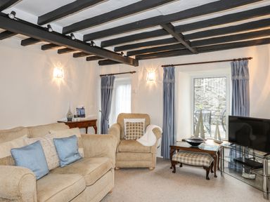 A living room with beige sofas blue curtains and a TV at Bwthyn Dwyfor in Beaumaris