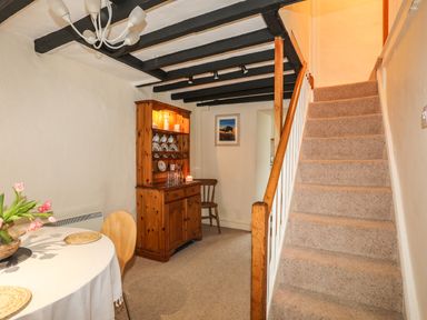 A dining area with a round table with flowers next to a wooden cabinet and carpeted stairs at Bwthyn Dwyfor in Beaumaris