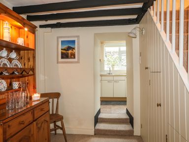 A hallway with wooden cupboard and chair next to a small stairway leading to a kitchen at Bwthyn Dwyfor in Beaumaris