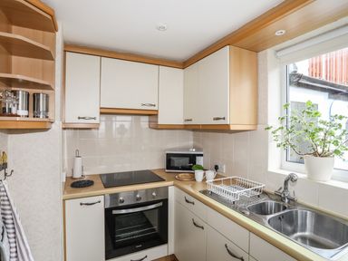 A kitchen with a stove oven microwave double sink and a potted plant on the windowsill at Bwthyn Dwyfor in Beaumaris