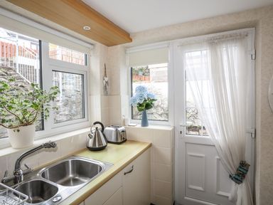 A kitchen sink with a kettle and toaster on the countertop next to a door and windows at Bwthyn Dwyfor in Beaumaris