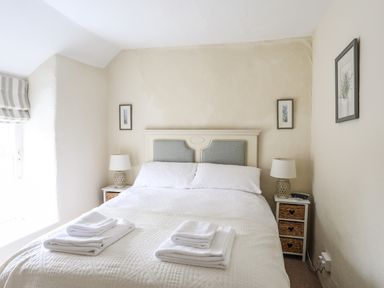 A bedroom with a double bed two bedside tables with lamps folded towels and framed pictures on walls at Bwthyn Dwyfor in Beaumaris