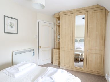 A bedroom with a bed folded towels a wooden wardrobe with a mirror and a white door at Bwthyn Dwyfor in Beaumaris