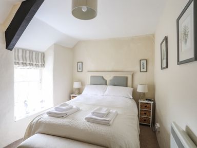 A bedroom with a double bed with white bedding two bedside tables with lamps and framed pictures on walls at Bwthyn Dwyfor in Beaumaris