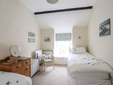 A bedroom with a single bed a chair a chest of drawers and a window with a patterned blind at Bwthyn Dwyfor in Beaumaris