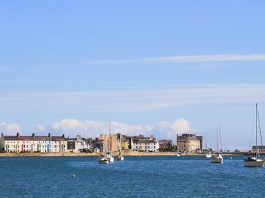 Boats floating on water with pastel colored houses and buildings along the shore at Bwthyn Dwyfor in Beaumaris