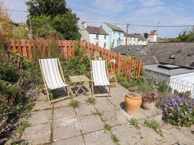 An outdoor patio area with two striped lounge chairs and a small table surrounded by plants and flowers at Bwthyn Dwyfor in Beaumaris