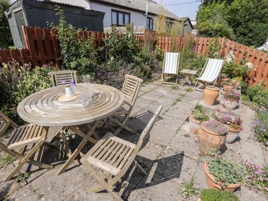 A garden patio with wooden table and chairs and potted plants at Bwthyn Dwyfor in Beaumaris