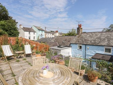 An outdoor patio with wooden table and chairs potted plants and deck chairs near houses at Bwthyn Dwyfor in Beaumaris
