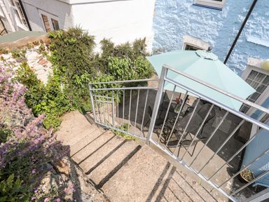 An outdoor patio area with a metal table and chairs under a blue umbrella viewed from stairs with plants around at Bwthyn Dwyfor in Beaumaris