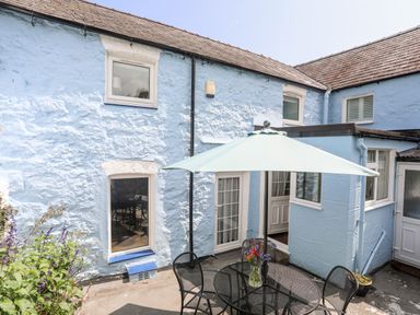 An outdoor patio area with a round table and umbrella beside a blue stone building at Bwthyn Dwyfor in Beaumaris