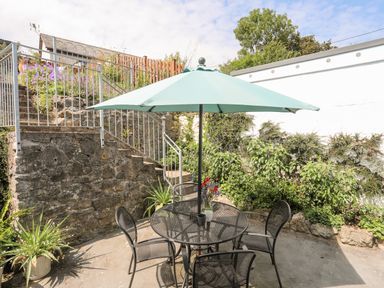 An outdoor patio with a round table and four chairs under a blue umbrella next to stone stairs and plants at Bwthyn Dwyfor in Beaumaris