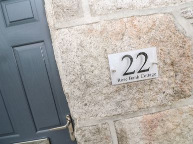 A stone wall with a sign displaying number 22 and Rose Bank Cottage next to a grey door at Rose Bank Cottage in St Just