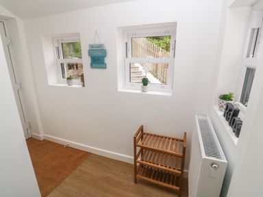 A hallway with three windows a wooden shoe rack a radiator and decorative signs at Rose Bank Cottage St Just
