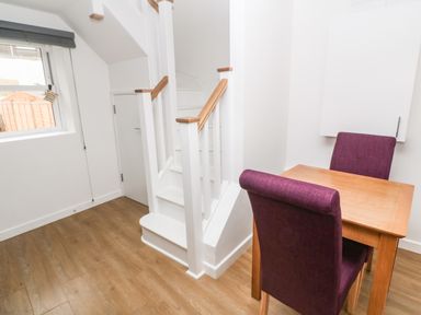 A small dining area with a wooden table and two purple chairs next to a white staircase and a window at Rose Bank Cottage in St Just