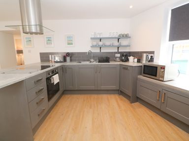 A kitchen with grey cabinets wooden floor a stove oven microwave and shelves with dishes at Rose Bank Cottage in St Just