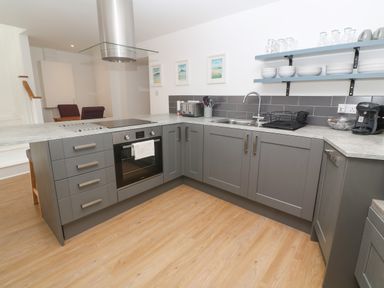 A kitchen with gray cabinets a built-in oven a sink and open shelves with dishes at Rose Bank Cottage in St Just