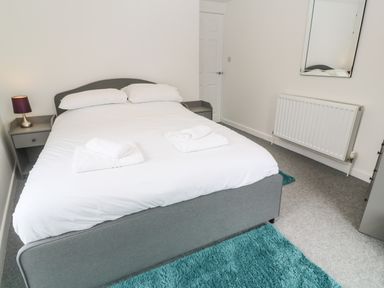 A bedroom with a double bed two bedside tables a lamp a mirror a radiator and a blue rug at Rose Bank Cottage in St Just