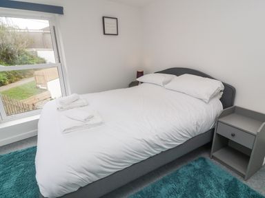 A bedroom with a double bed white bedding bedside table lamp window and a blue rug at Rose Bank Cottage in St Just