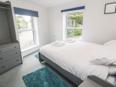 A bedroom with a double bed white bedding towels on the bed a dresser and two windows at Rose Bank Cottage St Just