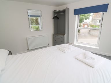 A bedroom with a bed, folded towels, an open wardrobe, a window with blue blinds and a wall mirror at Rose Bank Cottage in St Just