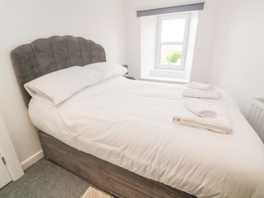 A bedroom with a large bed white bedding rolled towels and a window at Rose Bank Cottage in St Just