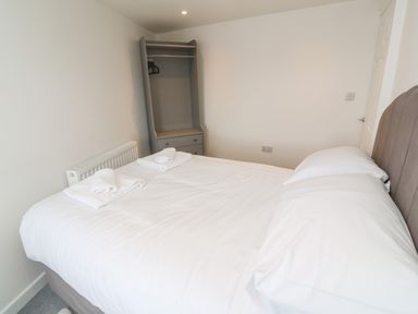 A bedroom with a bed with white bedding towels on the bed and an open wardrobe in Rose Bank Cottage in St Just