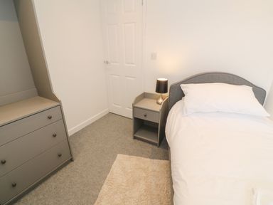 A bedroom with a bed a bedside table with a lamp a chest of drawers and a door at Rose Bank Cottage in St Just