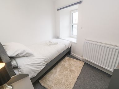 A small bedroom with a single bed a window radiator rug and bedside lamp at Rose Bank Cottage in St Just