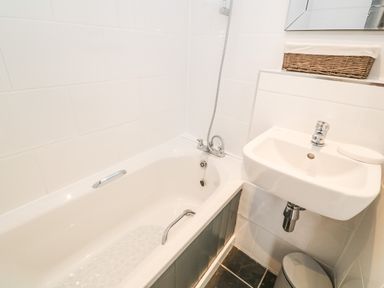 A bathroom with a bathtub shower sink with a wicker basket and a trash bin at Rose Bank Cottage in St Just