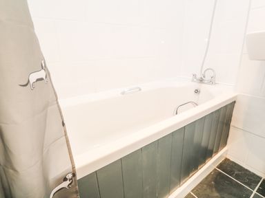 A bathtub with metal handles and a dog patterned shower curtain in a bathroom with tiled walls and floor at Rose Bank Cottage in St Just