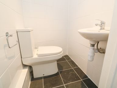 A small bathroom with a toilet and a wall-mounted sink with black tiled floor