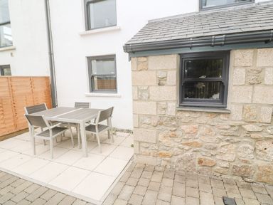 An outdoor patio area with a table and four chairs next to a stone and white wall at Rose Bank Cottage in St Just
