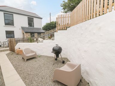 An outdoor patio area with two beige chairs a black charcoal grill gravel ground and white walls
