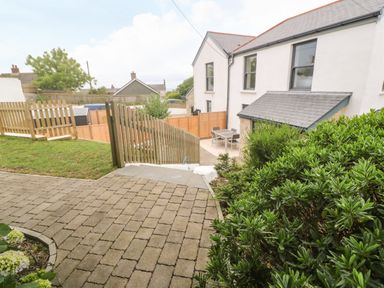 A backyard with paved pathway and green bushes near a white two-story house at Rose Bank Cottage in St Just
