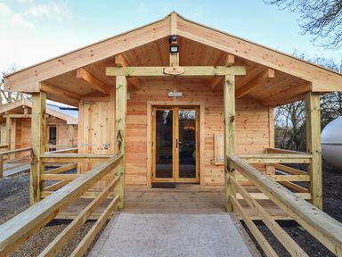 A wooden cabin with a porch and railing at Buttercup Lodge in Theberton near Leiston