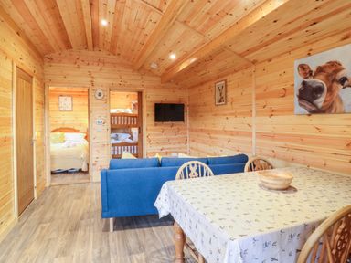 An interior room with wooden walls and ceiling a blue sofa a dining table with chairs and paintings on the walls at Buttercup Lodge in Theberton near Leiston