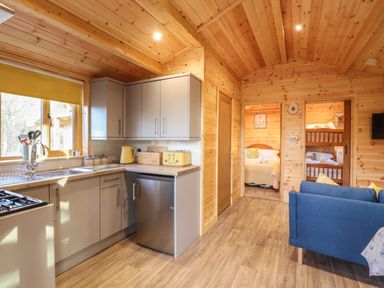 A kitchen with grey cabinets and yellow appliances next to a living area with a blue sofa at Buttercup Lodge in Theberton near Leiston