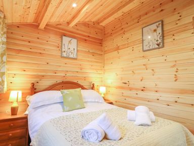 A bedroom with a bed folded towels bedside tables with lamps and wooden walls at Buttercup Lodge in Theberton near Leiston