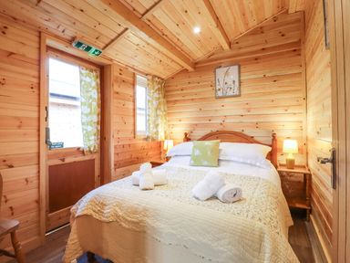 A bedroom with a double bed bedside tables and a door with floral curtains at Buttercup Lodge Theberton near Leiston