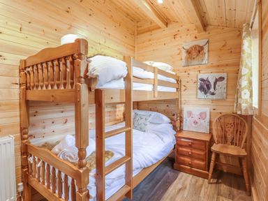 A wooden bunk bed with white bedding next to a wooden nightstand and chair in a wooden room at Buttercup Lodge in Theberton near Leiston