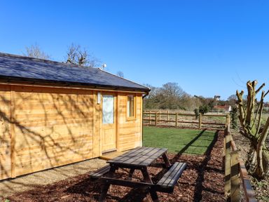 A wooden cabin with a picnic table outside and fenced green grass at Buttercup Lodge in Theberton near Leiston