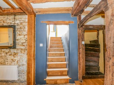 A stone wall with a mirror radiator and wooden beams with two staircases one wooden and modern the other older and darker at Fox Den Cottage in Castle Combe