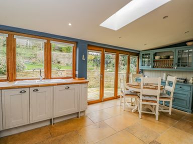 A kitchen with white cabinets a wooden countertop a round dining table with four chairs and glass doors leading to a garden at Fox Den Cottage in Castle Combe