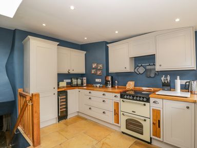 A kitchen with cream cabinets wooden countertops and a cream oven at Fox Den Cottage in Castle Combe