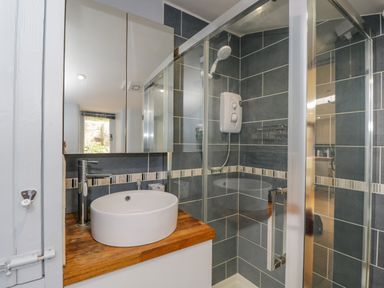 A bathroom with a round sink on a wooden countertop and a glass-enclosed shower at Fox Den Cottage in Castle Combe