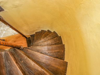 A spiral wooden staircase with a handrail next to a yellow wall at Fox Den Cottage in Castle Combe